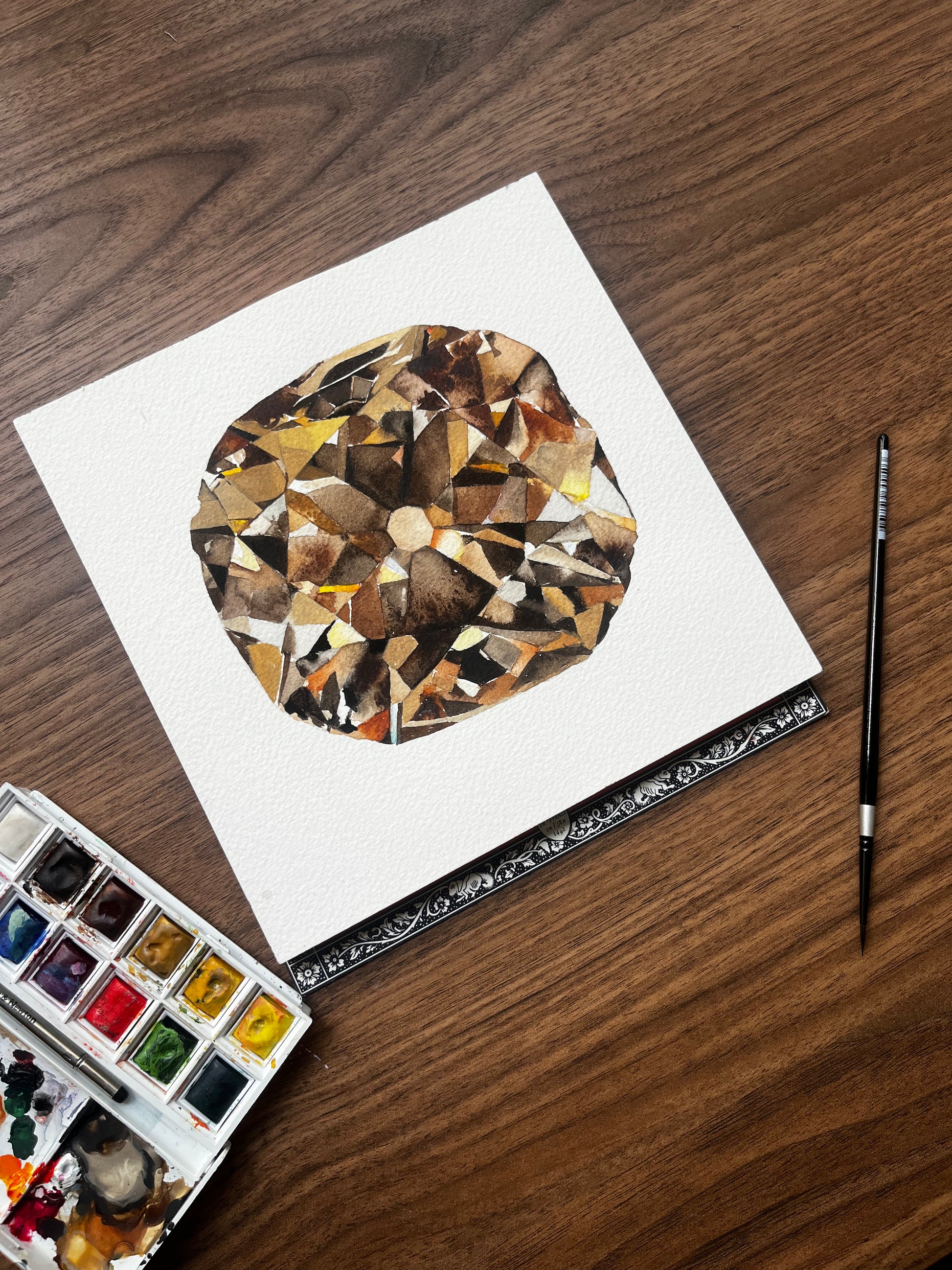 Artistic depiction of a diamond on paper with watercolor paints and brush on a wooden surface